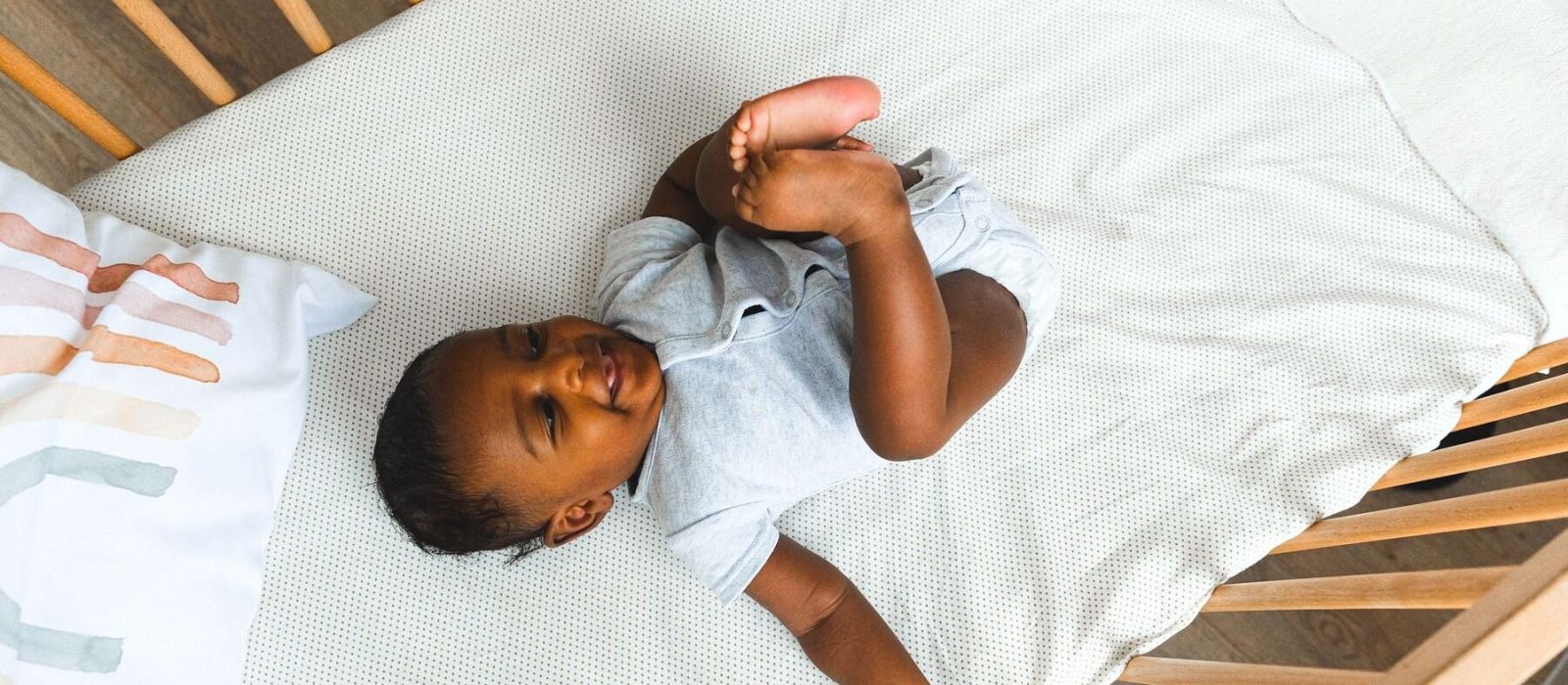 Lachende baby ligt wakker in het ledikant, gezien van boven